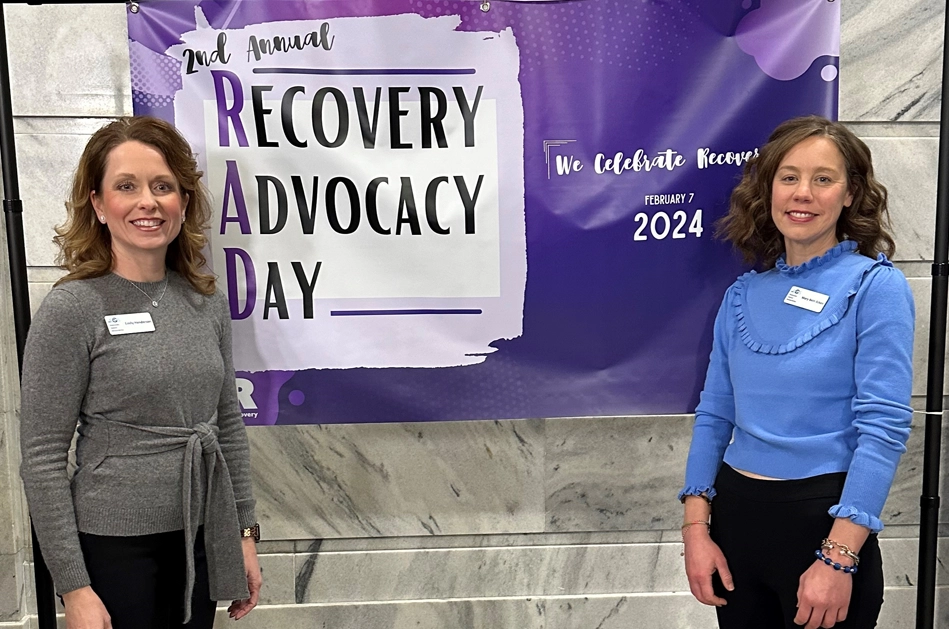 KHA's Emily Henderson and Mary Beth Ecken standing in front of a banner promoting Annual Recovery Advocacy Day